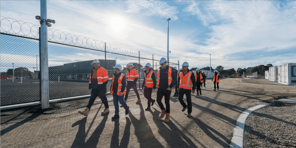 Group in safety gear touring fenced industrial site under sunny sky.